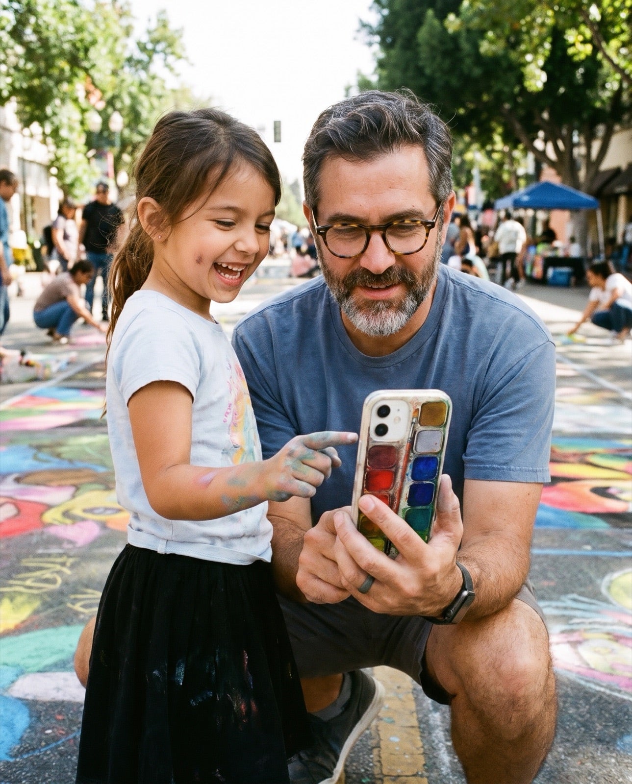 A girl with chalky hands pointing at her dad's watercolor phone case at a chalk festival